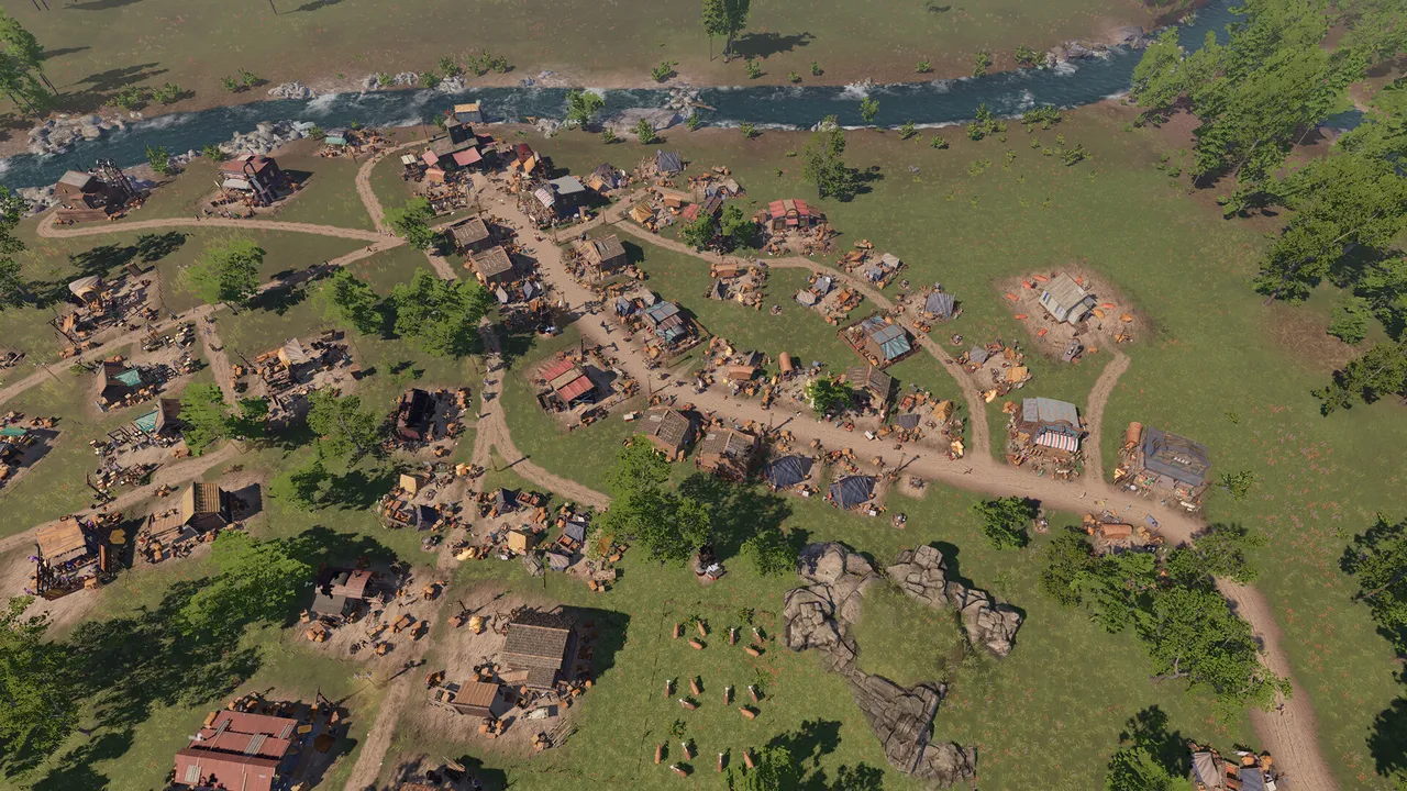 A frontier town of cabins and dirt roads beside a river, seen from above